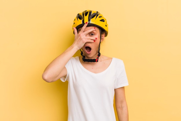 Junge hübsche Frau, die schockiert, verängstigt oder verängstigt aussieht und das Gesicht mit Handbike-Konzept bedeckt