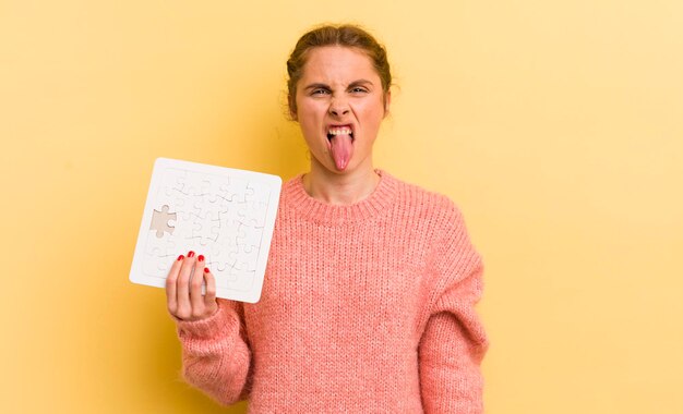 Junge hübsche Frau, die sich angewidert und gereizt fühlt und ein Puzzle-Konzept mit herausgestreckter Zunge hat