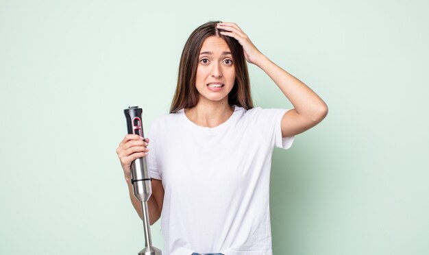 Junge hübsche Frau, die sich gestresst, ängstlich oder verängstigt fühlt, mit den Händen auf dem Kopf. Handmixer-Konzept