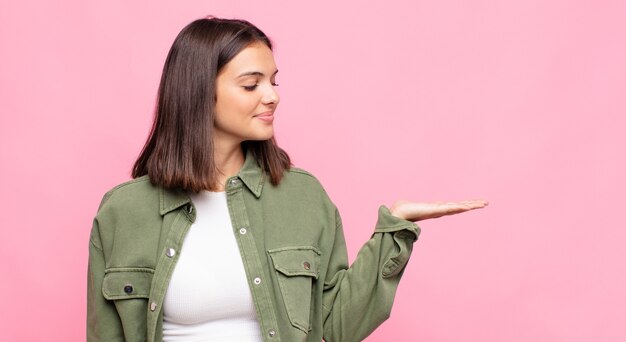 Junge hübsche Frau, die sich glücklich fühlt und beiläufig lächelt und auf ein Objekt oder Konzept schaut, das auf der Hand auf der Seite gehalten wird