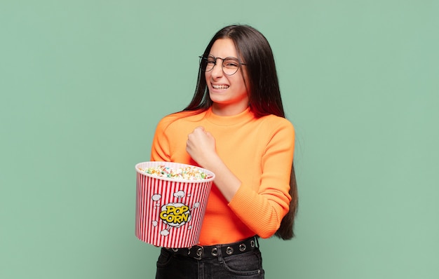 Junge hübsche Frau, die sich glücklich, positiv und erfolgreich fühlt, motiviert, wenn sie sich einer Herausforderung stellt oder gute Ergebnisse feiert. Popcorn-Konzept