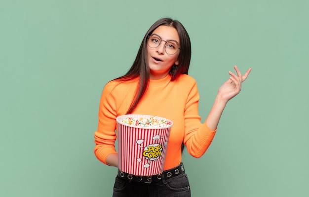 Junge hübsche Frau, die sich glücklich, überrascht und fröhlich fühlt, mit positiver Einstellung lächelt und eine Lösung oder Idee realisiert. Popcorn-Konzept