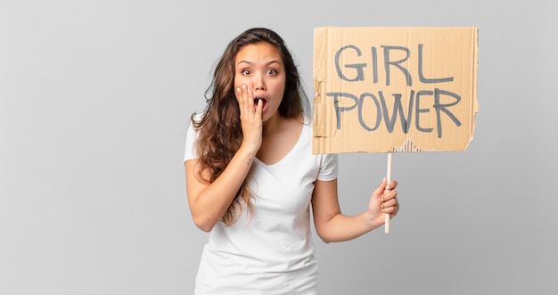 Junge hübsche Frau, die sich schockiert und verängstigt fühlt und ein Girl-Power-Banner hält