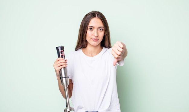 Junge hübsche frau, die sich überquert und daumen nach unten zeigt. handmixer-konzept