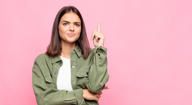 Junge hübsche Frau, die sich wie ein Genie fühlt, das stolz Finger in der Luft hält