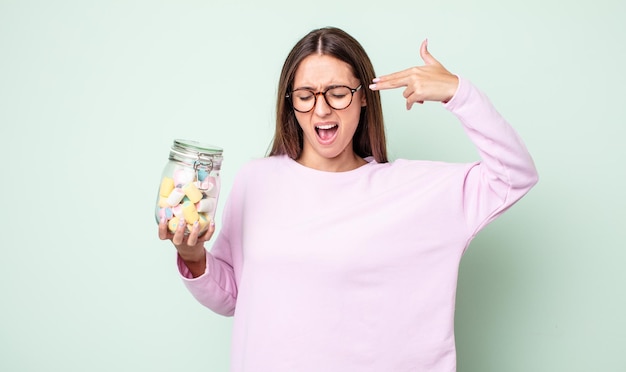 Junge hübsche Frau, die unglücklich und gestresst aussieht, Selbstmordgeste, die Waffenzeichen macht. Gelee Bonbons Konzept