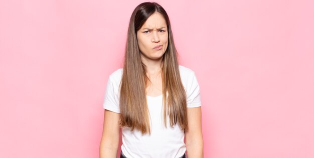 Junge hübsche Frau, die verwirrt und zweifelnd ist, sich wundert oder versucht, eine Entscheidung zu treffen