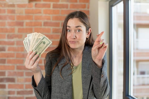 junge hübsche Frau drückt die Daumen und hofft auf viel Glück Dollar-Banknoten-Konzept