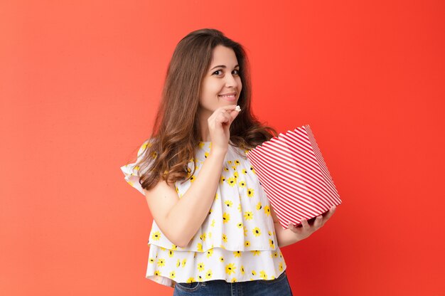 Junge hübsche Frau gegen rote Wand mit einem Popcorn-Eimer