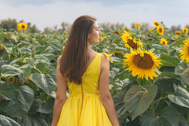 Junge hübsche Frau im gelben Kleid unter dem Sonnenblumenfeld im Sommer. Bereza, Weißrussland.