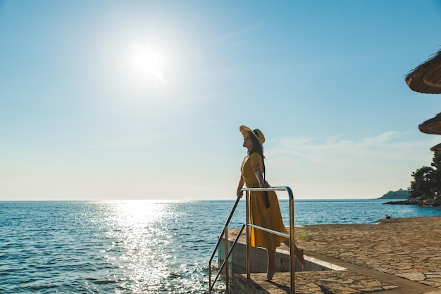 Junge hübsche Frau im gelben Sommerkleid am Meeresstrand