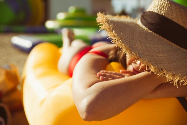 Junge hübsche frau im roten badeanzug am gelben luftsofa in den sommerferien am meerstrand