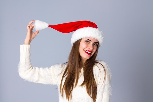 Junge hübsche Frau im weißen Pullover mit roter Weihnachtsmütze, die Bubo auf grauem Hintergrund im Studio hält