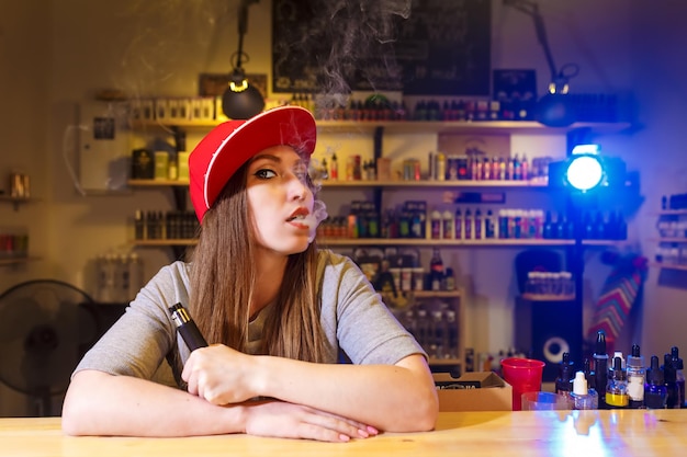 Junge hübsche frau in der roten kappe rauchen eine elektronische zigarette am vape shop