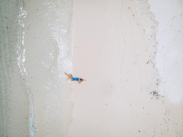 Junge hübsche Frau in einem blauen Badeanzug, der während der Flut an einem Sandstrand liegt. Sommerferienkonzept
