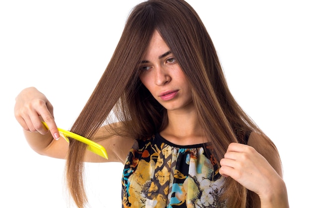 Junge hübsche Frau in farbigem Hemd, die ihr langes braunes Haar mit gelber Haarbürste im Studio kämmt