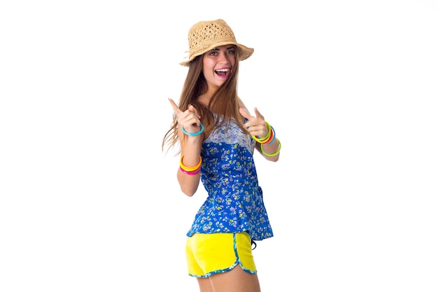 Junge hübsche Frau in Shorts mit farbigen Armbändern und Hut lächelt und hält ihr Bein hoch