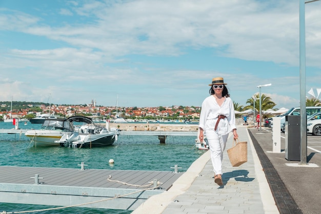 Junge hübsche Frau in weißer Sommerkleidung, die am Yachtdock vorbeigeht