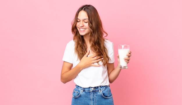 Junge hübsche Frau lacht laut über einen lustigen Witz und hält ein Glas Milch