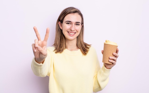 Junge hübsche Frau lächelt und sieht glücklich aus und gestikuliert Sieg oder Frieden zum Mitnehmen des Kaffeekonzepts