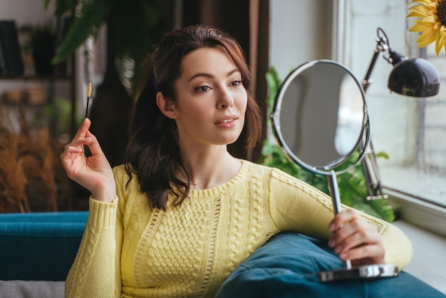 Junge hübsche Frau macht Make-up zu Hause, während sie in den Spiegel schaut