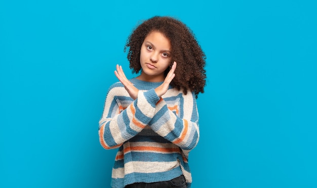 junge hübsche Frau mit Afro-Haar und gestreiftem Pullover, der auf blauer Wand aufwirft