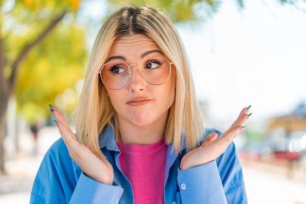 Foto junge hübsche frau mit brille im freien macht zweifel geste