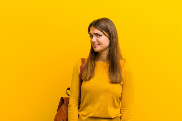 Junge hübsche Frau mit einem albernen, verrückten, überraschten Ausdruck, Puffwangen, sich gestopft, fett und voller Essen vor orange Hintergrund fühlen