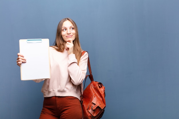 Junge hübsche Frau mit einem Blatt Papier gegen blaue Wand mit einem copyspace