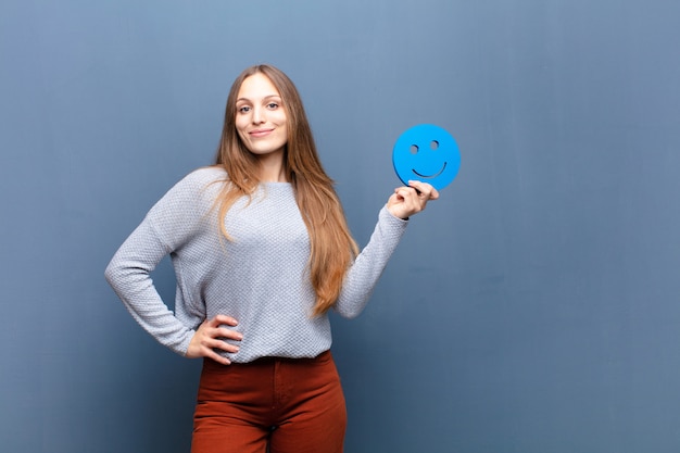 Junge hübsche Frau mit einer blauen Wand des lächelnden Gesichtes mit einem Kopienraum