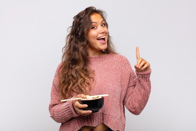 Junge hübsche Frau mit Nudeln, die sich wie ein glückliches und aufgeregtes Genie fühlen, nachdem sie eine Idee verwirklicht haben, fröhlich Finger heben, Eureka!