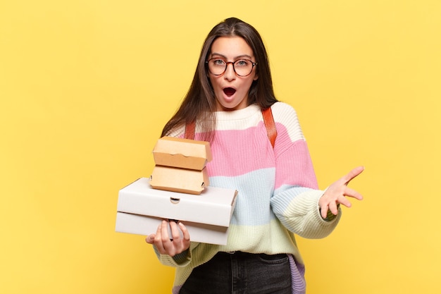 Junge hübsche Frau mit offenem Mund und erstaunt, schockiert und erstaunt mit einer unglaublichen Überraschung. Nehmen Sie ein Fast-Food-Konzept