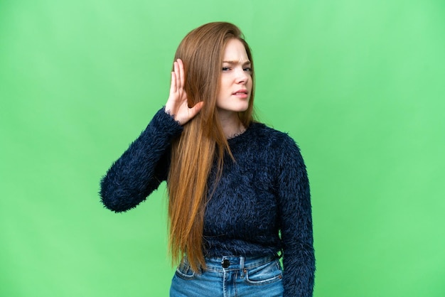 Junge hübsche Frau vor isoliertem Chroma-Key-Hintergrund, die etwas hört, indem sie die Hand auf das Ohr legt