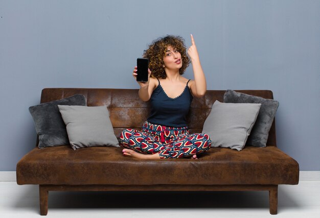 Foto junge hübsche frau zu hause, mit einem handy, pyjama auf einem sofa tragend