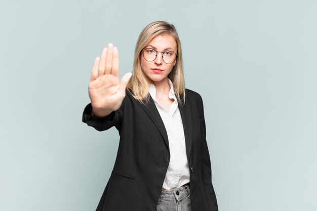 Junge hübsche Geschäftsfrau, die ernst, streng, unzufrieden und wütend aussieht und offene Handfläche zeigt, die eine Stopp-Geste macht