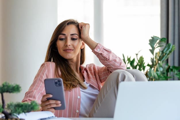 Junge hübsche Geschäftsfrau im Büro, die im Bürostuhl sitzt und auf ihrem Smartphone spricht