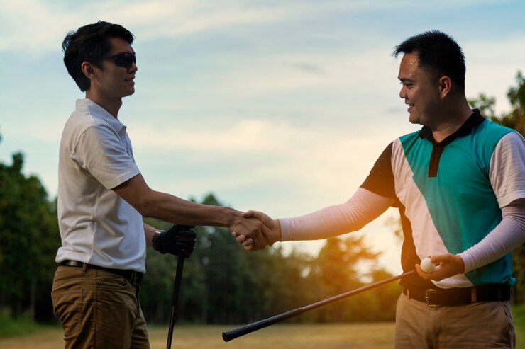 Junge hübsche Geschäftsmannschüttelnhände auf dem Golf
