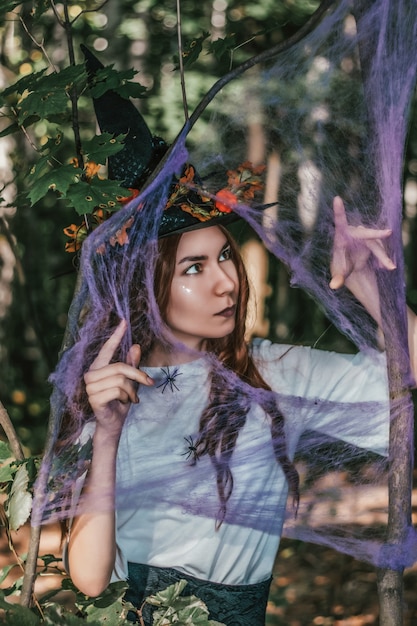 Junge hübsche Hexe im schwarzen Hut hautnah im Wald. Welches Halloween-Cosplay. Kunstverarbeitung.