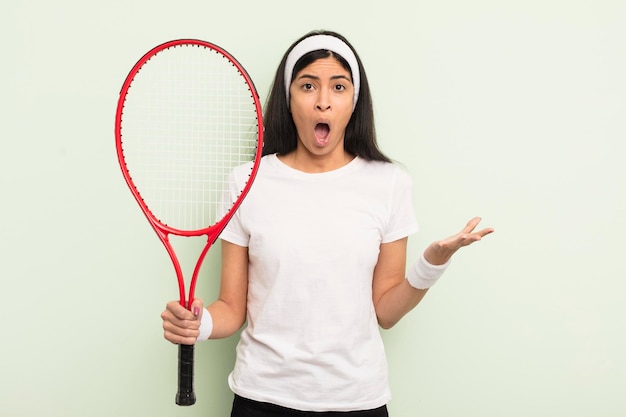 Junge hübsche hispanische Frau, die sich extrem schockiert und überrascht über das Tenniskonzept fühlt