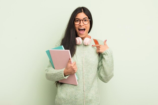 Junge hübsche hispanische Frau, die sich glücklich fühlt und mit einem aufgeregten Studentenkonzept auf sich selbst zeigt