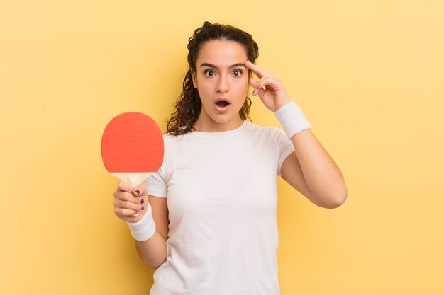 Junge hübsche hispanische Frau, die überrascht aussieht und einen neuen Gedanken, eine neue Idee oder ein neues Konzept verwirklicht. Ping-Pong-Konzept