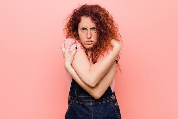 Junge hübsche Ingwer-Rotschopf-Frau, die eine Jeans-Latzhose trägt, die wegen niedriger Temperatur kalt wird