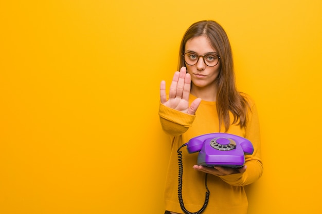 Junge hübsche kaukasische Frau, die Hand in Front einsetzt. Sie hält ein altes Telefon in der Hand.