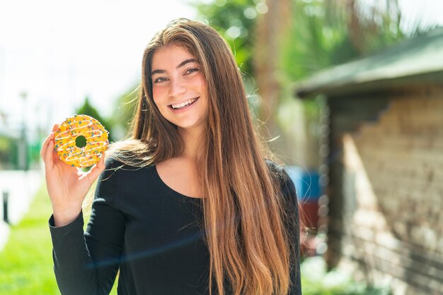 Junge hübsche kaukasische Frau hält einen Donut im Freien und lächelt viel