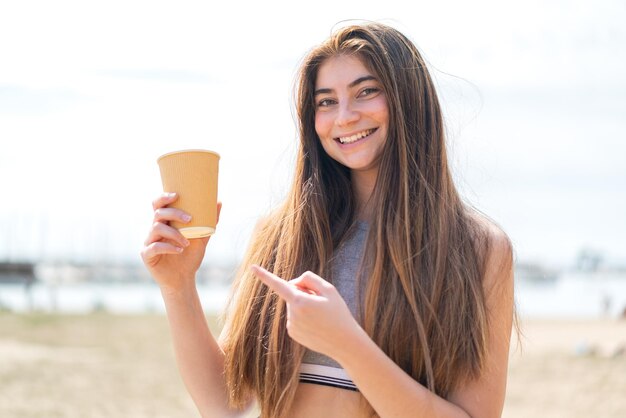 Junge hübsche kaukasische Frau hält einen Take-Away-Kaffee im Freien und zeigt ihn