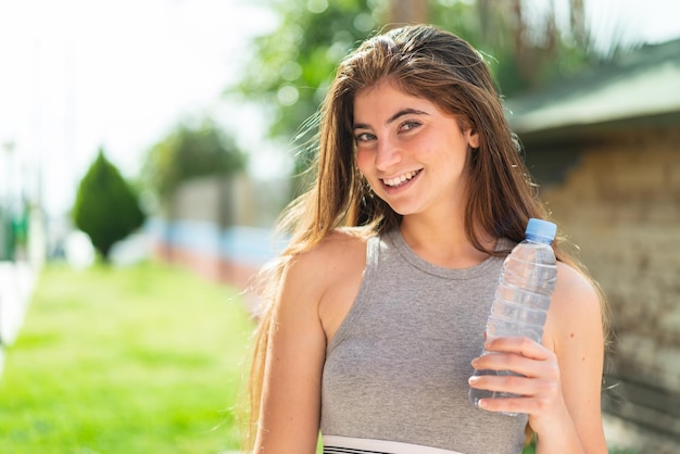 Junge hübsche kaukasische Frau mit einer Flasche Wasser im Freien, die viel lächelt