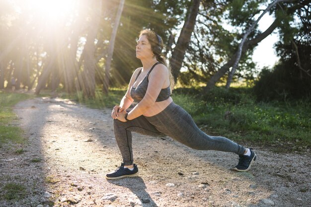 Junge hübsche lächelnde Frau in Übergröße in sportlichem Oberteil und Leggings, die Sport treibt und Musik hört