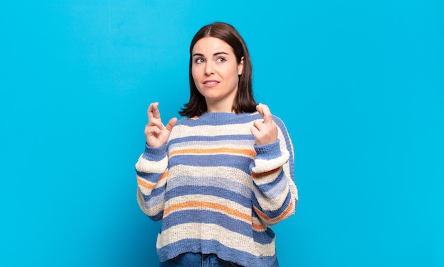 Junge hübsche lässige Frau, die ängstlich die Finger kreuzt und auf Glück mit einem besorgten Blick hofft