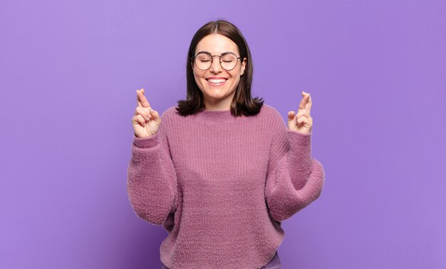 junge hübsche lässige Frau, die nervös und hoffnungsvoll ist, die Daumen drückt, betet und auf viel Glück hofft