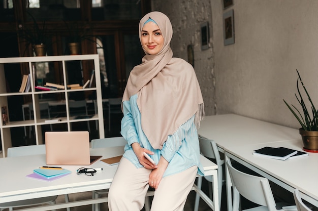 Junge hübsche moderne muslimische Frau im Hijab, die im Büroraum arbeitet, Bildung online